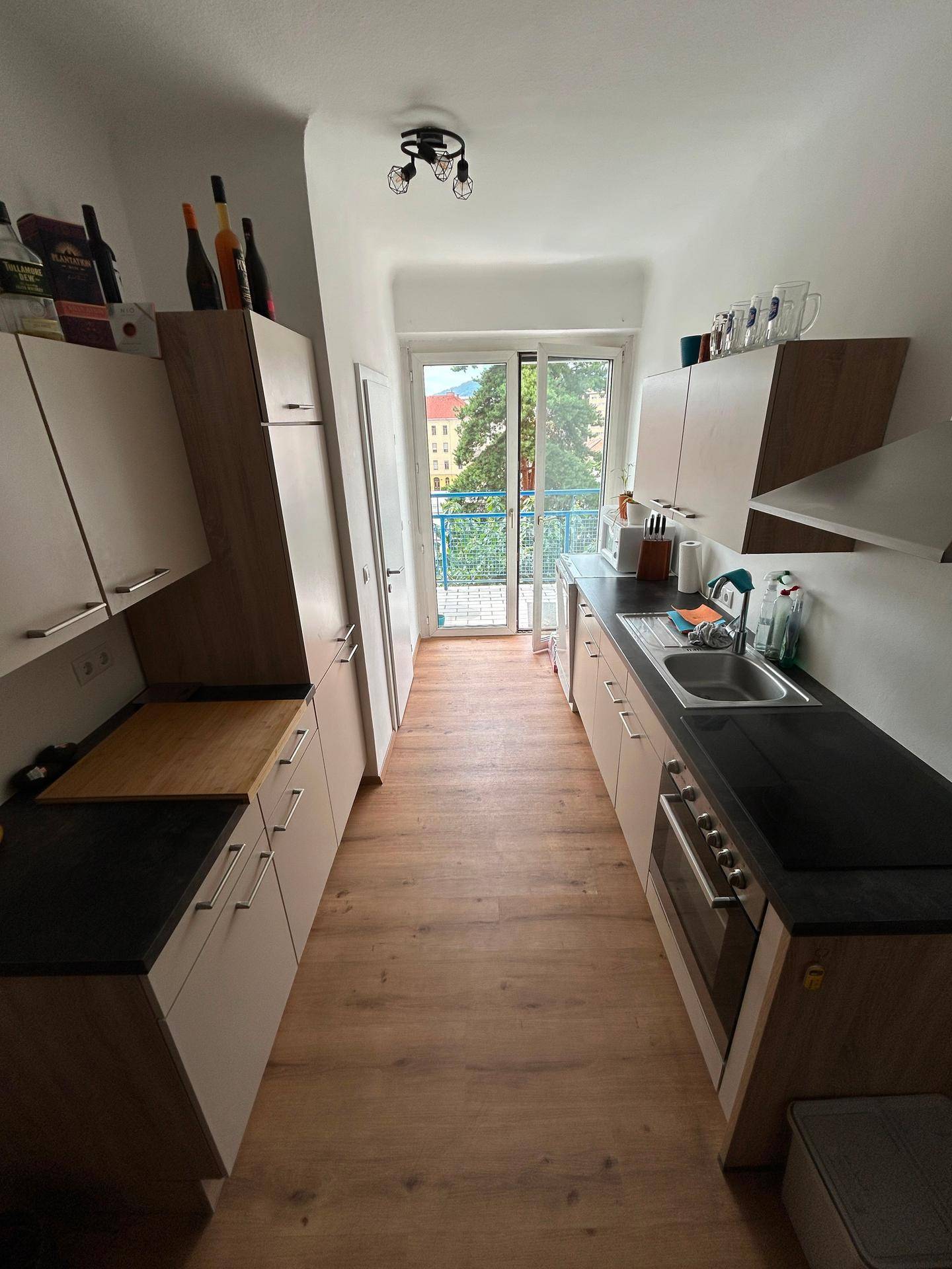 Funktionale Küche mit hellen Schränken, dunkler Arbeitsplatte und direktem Zugang zum Balkon.