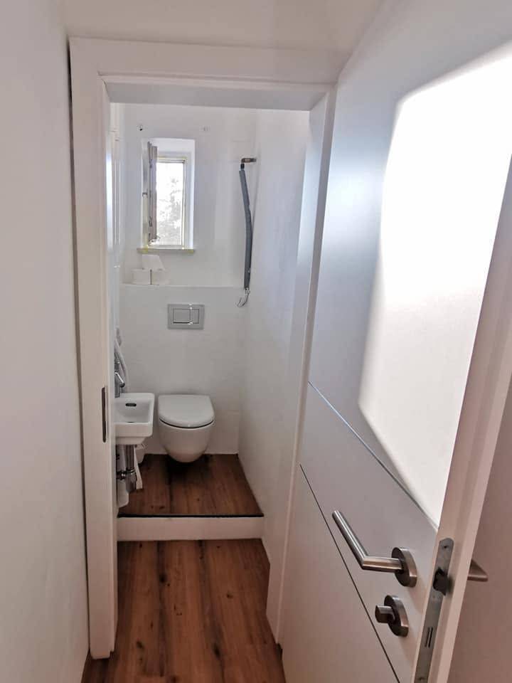 Kleines Gäste-WC mit Fenster, wandhängendem WC und kleinem Waschbecken.