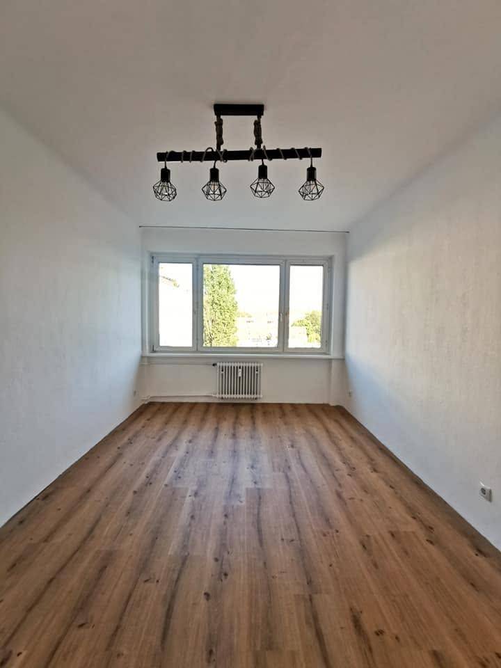 Heller, leerer Raum mit Holzboden, großem Fenster und Heizkörper, bereit zur Einrichtung.