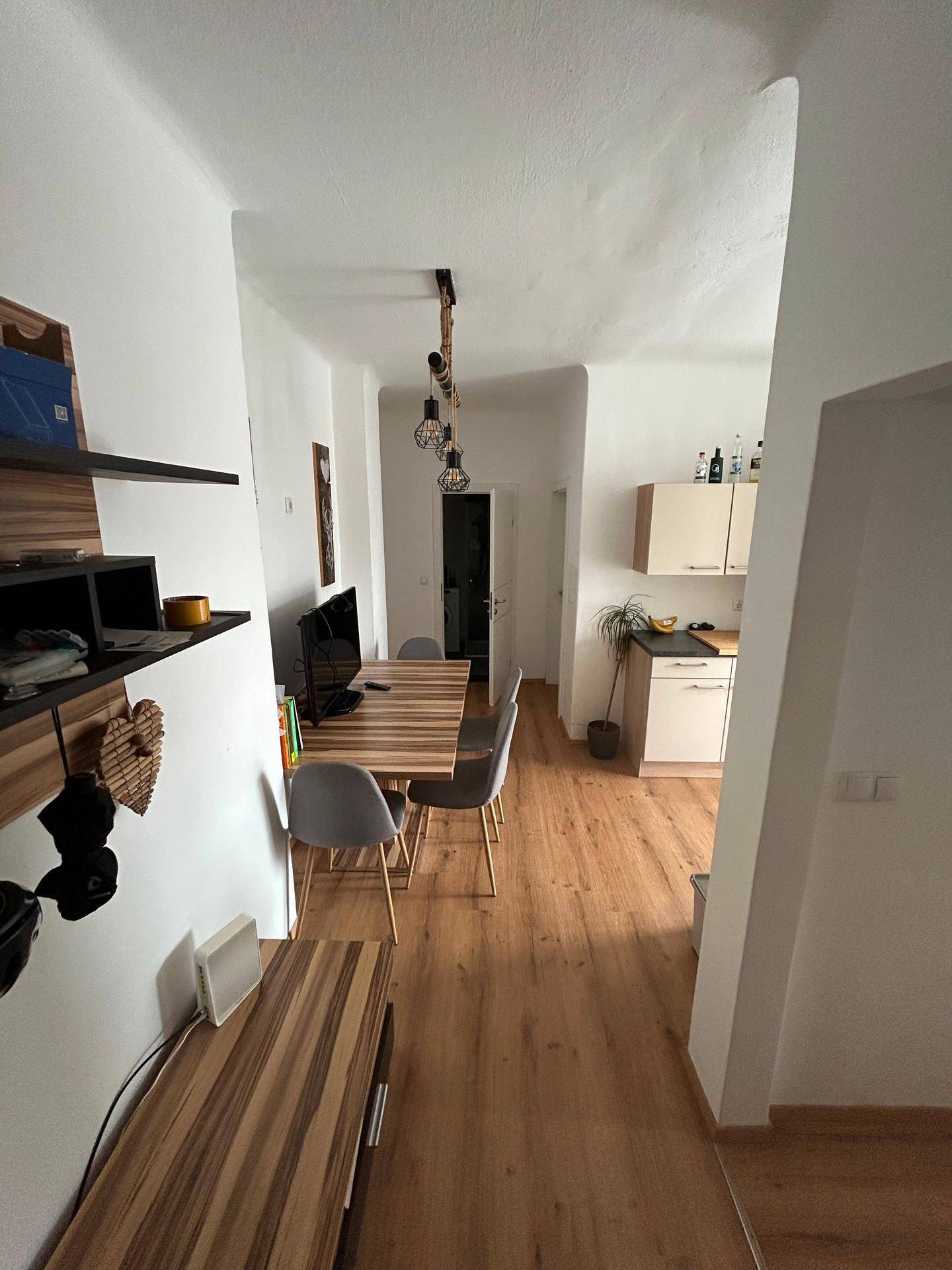 Heller Essbereich mit Holztisch und Regalen, der in eine kleine Küche übergeht.