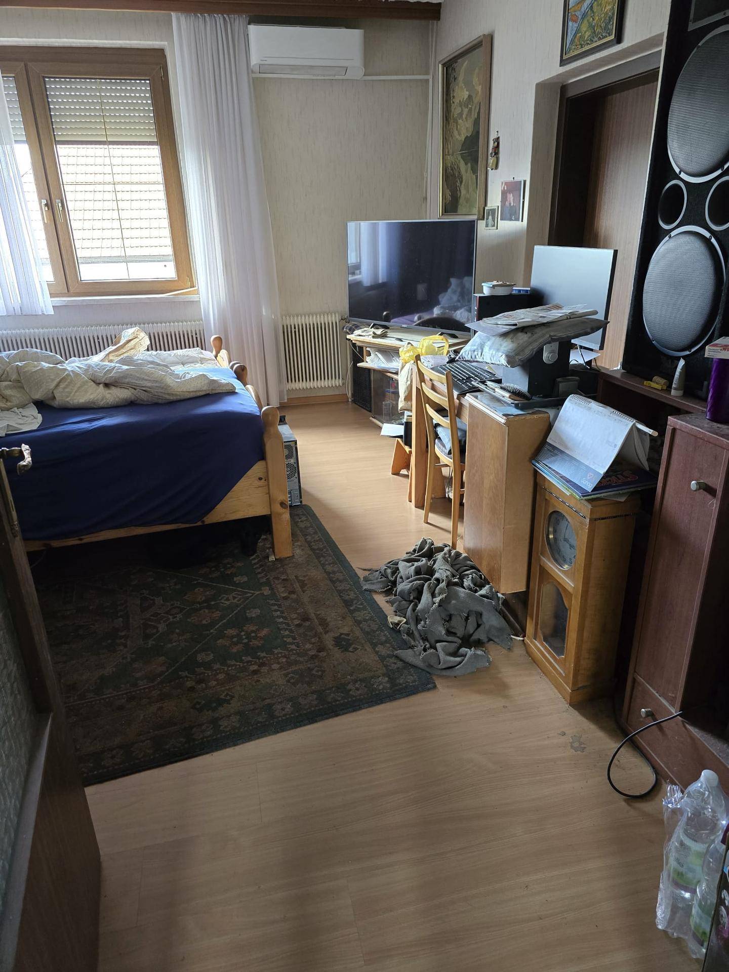 Schlafzimmer mit Bett, Schreibtisch, Fernseher und einer Klimaanlage an der Wand.