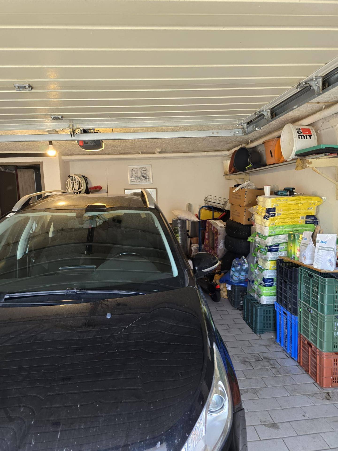 Geräumige Garage mit einem geparkten Auto und Regalen für Lagerung und verschiedene Gegenstände.