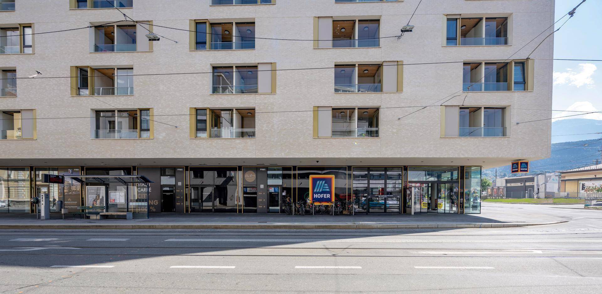 Modernes Gebäude mit großen Fenstern und Einzelhandelsflächen im Erdgeschoss an einer belebten Straße.