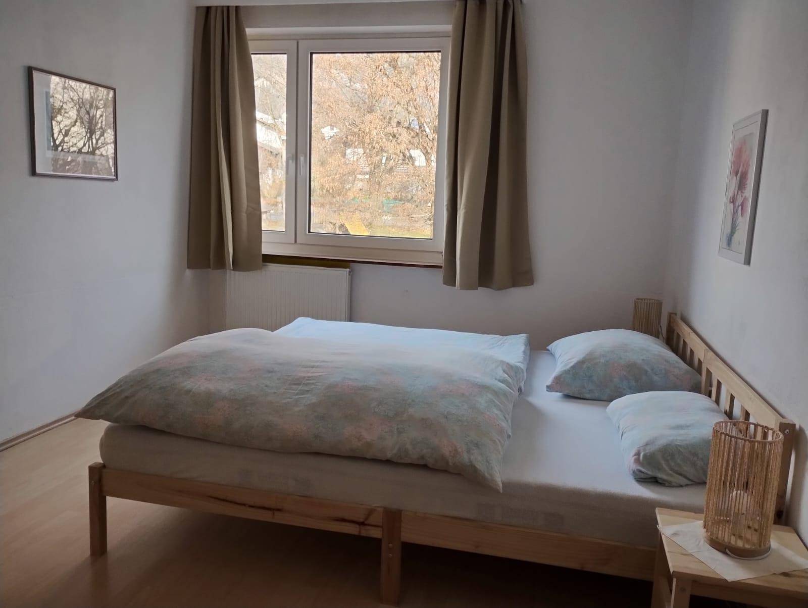Schlafzimmer mit Holzbett, Parkettboden und großem Fenster für viel Tageslicht.