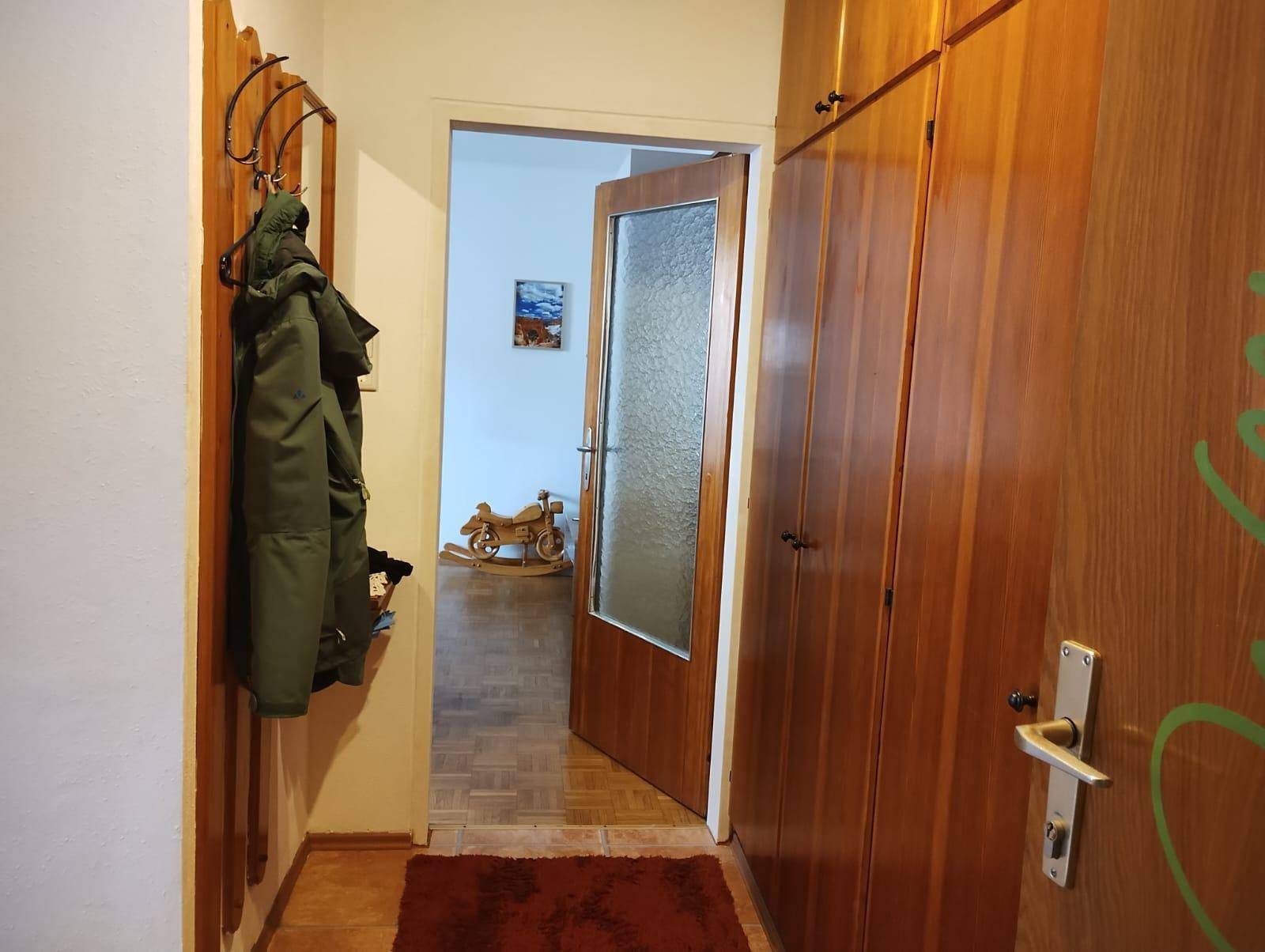 Schmaler Flur mit Holzschränken und Garderobe, der zu weiteren Räumen führt.