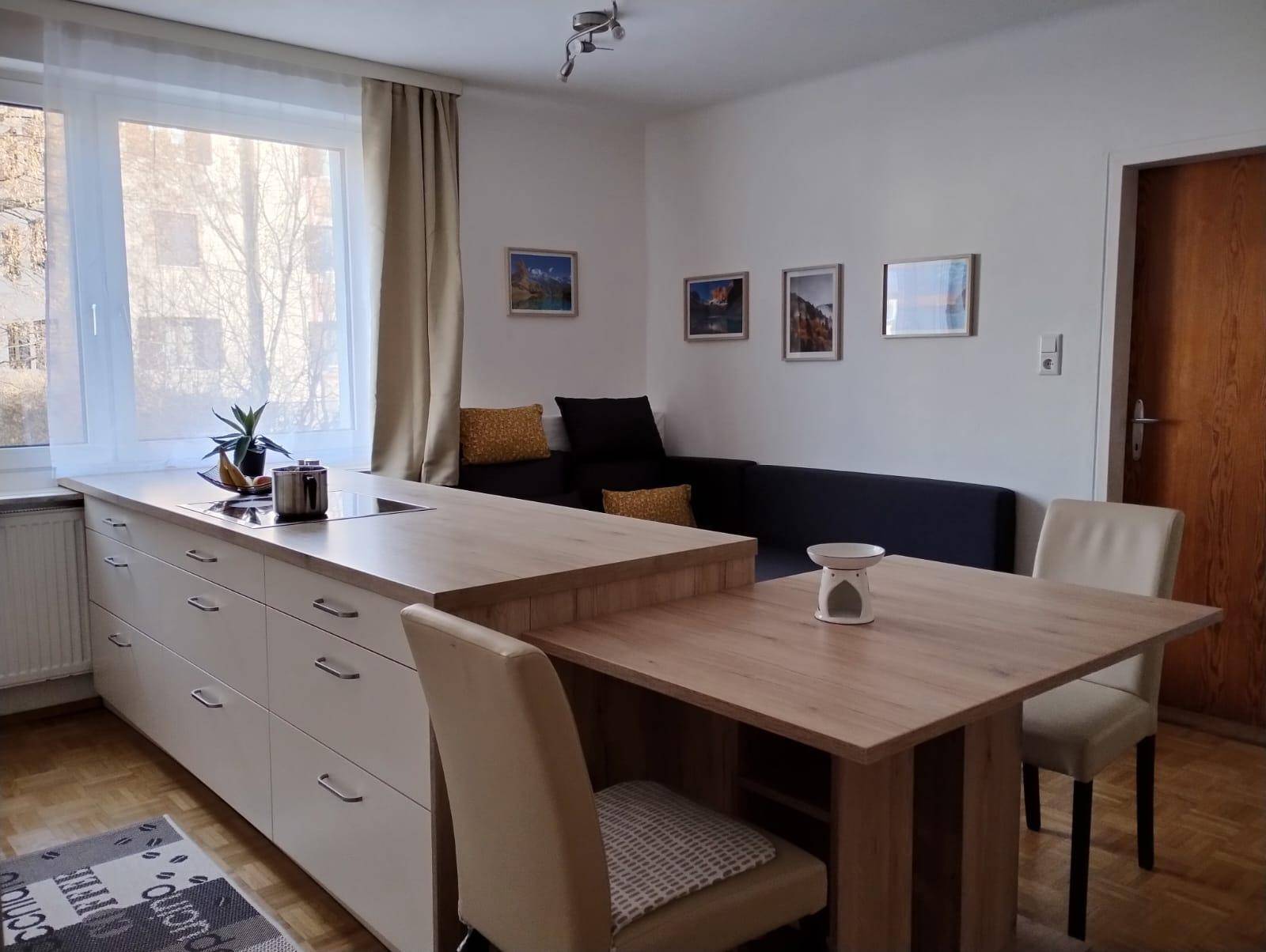 Heller Wohn- und Essbereich mit Kücheninsel, Sofa und Blick nach draußen.