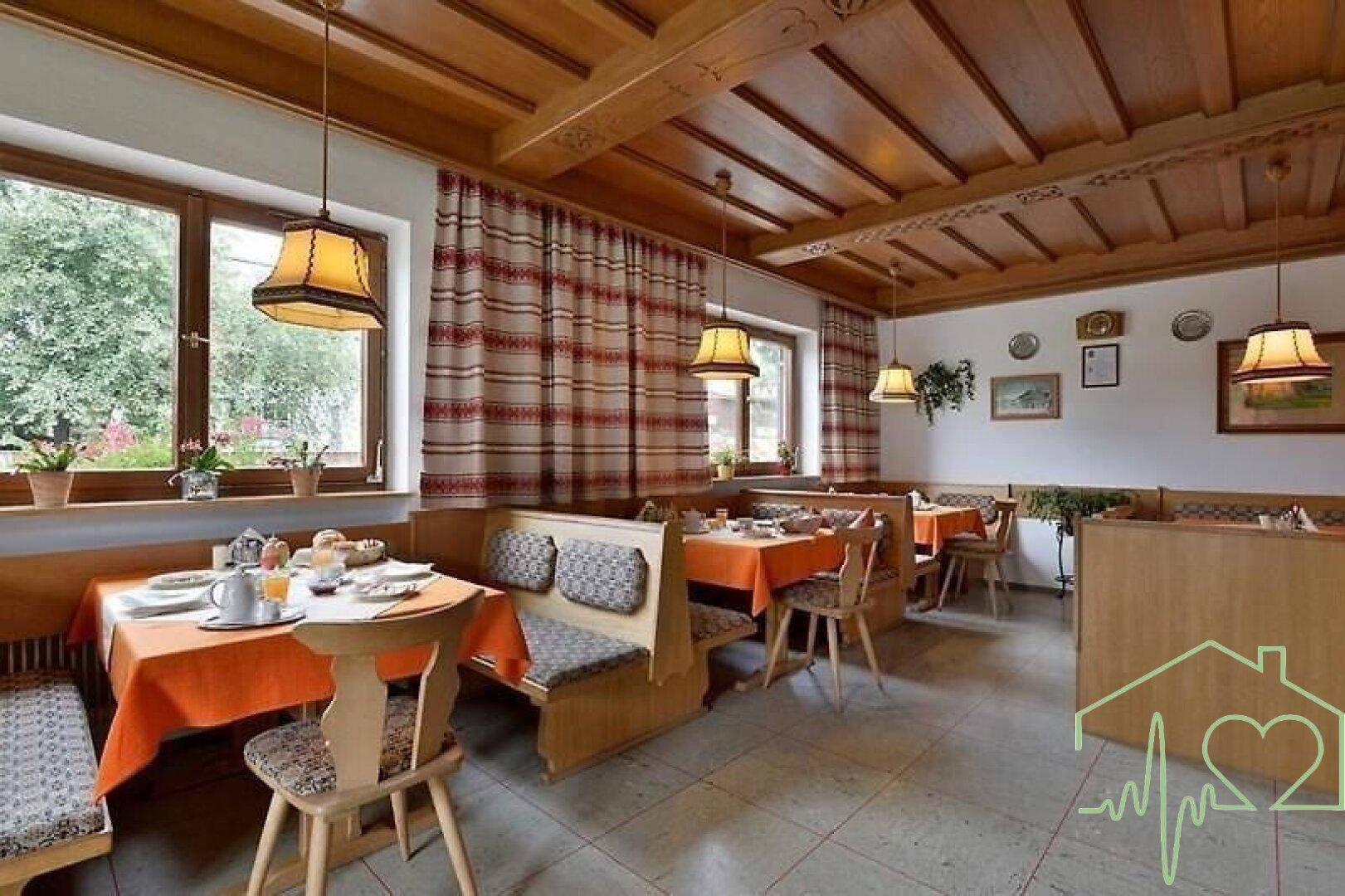 Traditioneller Speisesaal mit Holztäfelung, Holzbalkendecke und mehreren Esstischen.