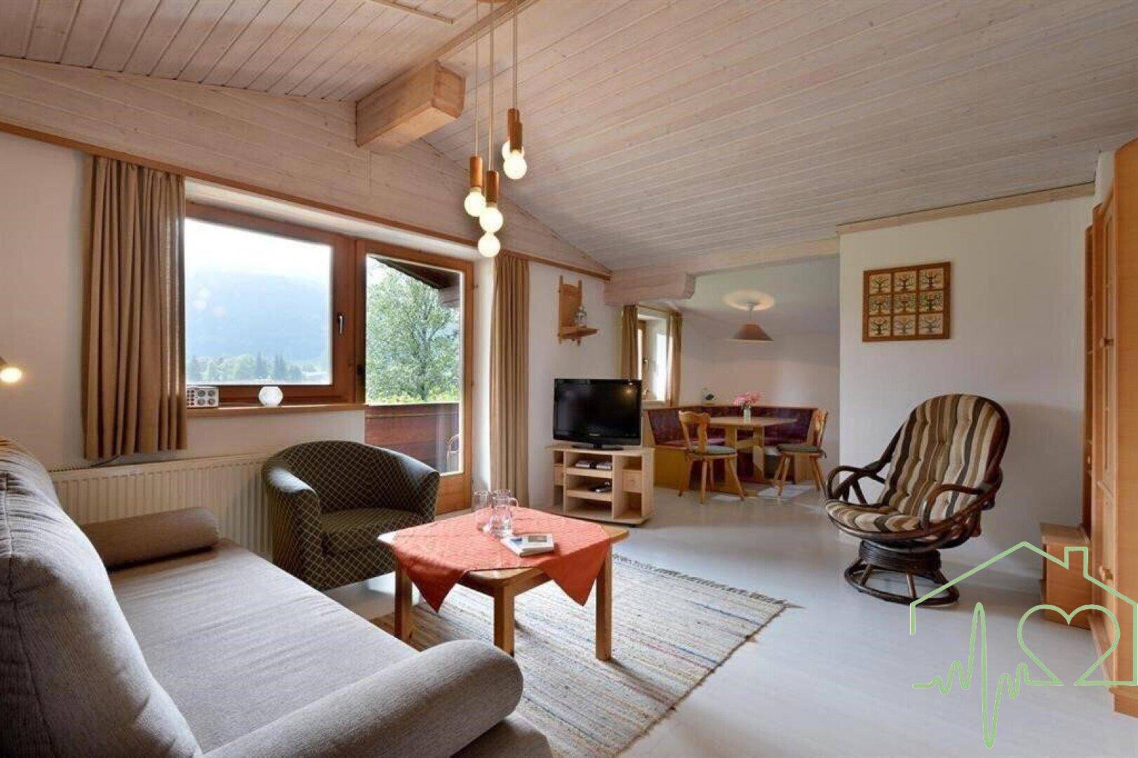 Heller Wohn-Essbereich mit Holzboden, Holzbalkendecke und Bergblick durch große Fenster.