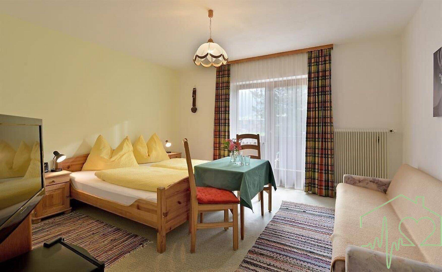 Gemütliches Schlafzimmer mit Doppelbett, Sofa und kleinem Tisch, hell und traditionell eingerichtet.