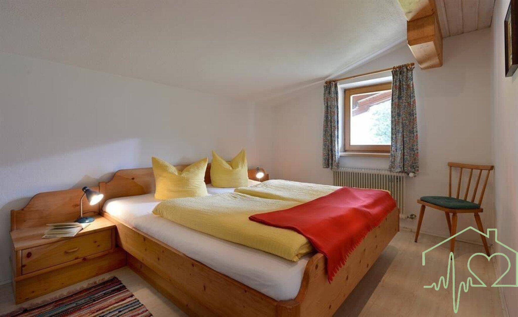 Helles Schlafzimmer mit Doppelbett, Holzmöbeln und schrägen Decken im Dachgeschoss.