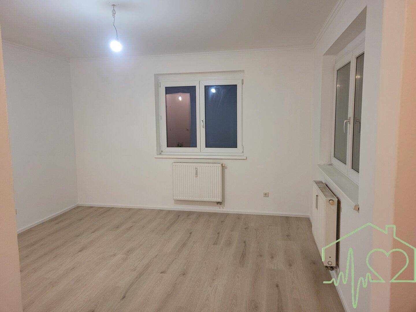 Lichtdurchfluteter Raum mit zwei Fenstern, Heizkörpern und hellem Laminatboden, bereit zur Einrichtung.