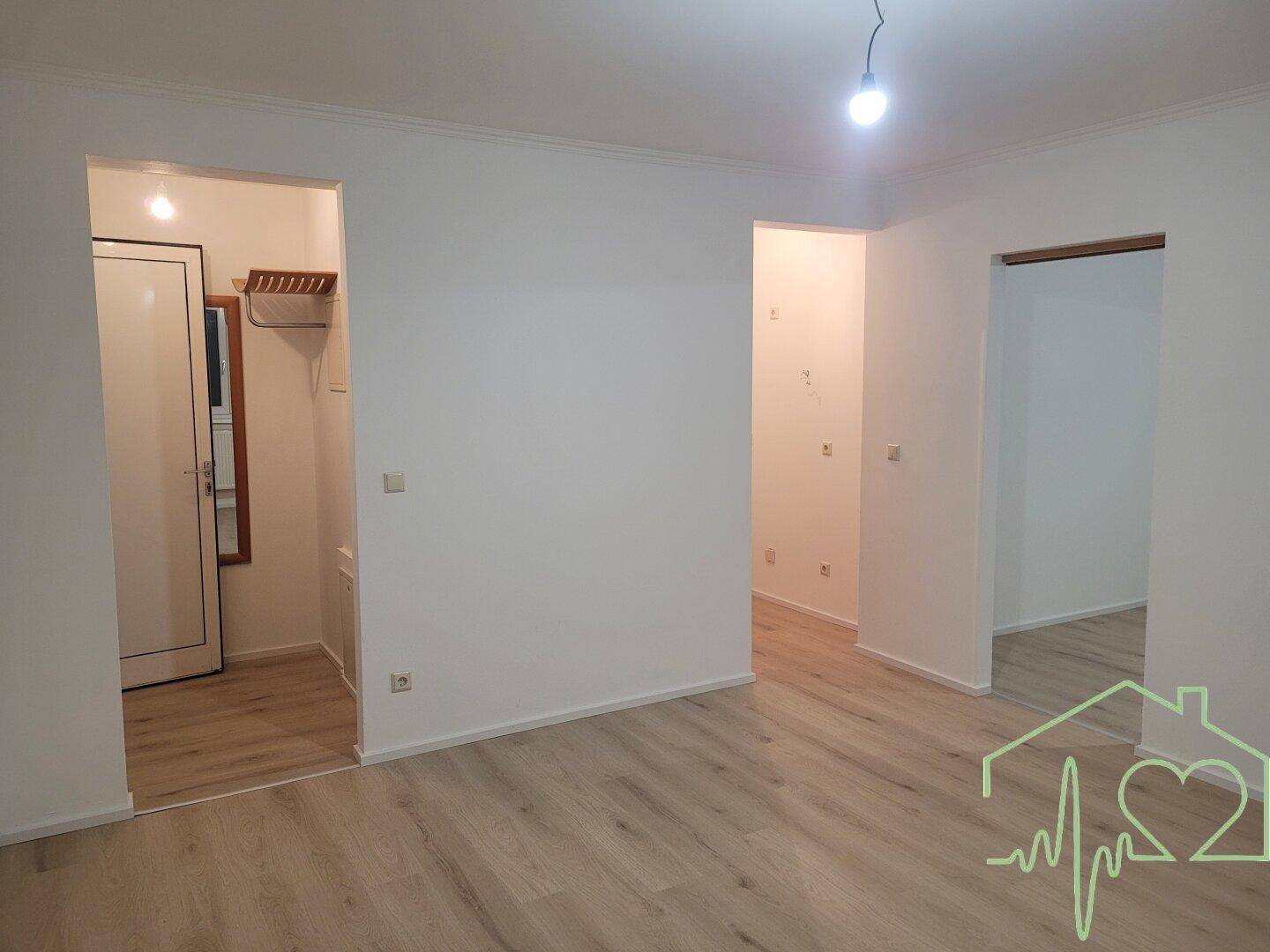 Geräumiger, leerer Wohnraum mit hellem Laminatboden und mehreren Türöffnungen zu angrenzenden Zimmern.