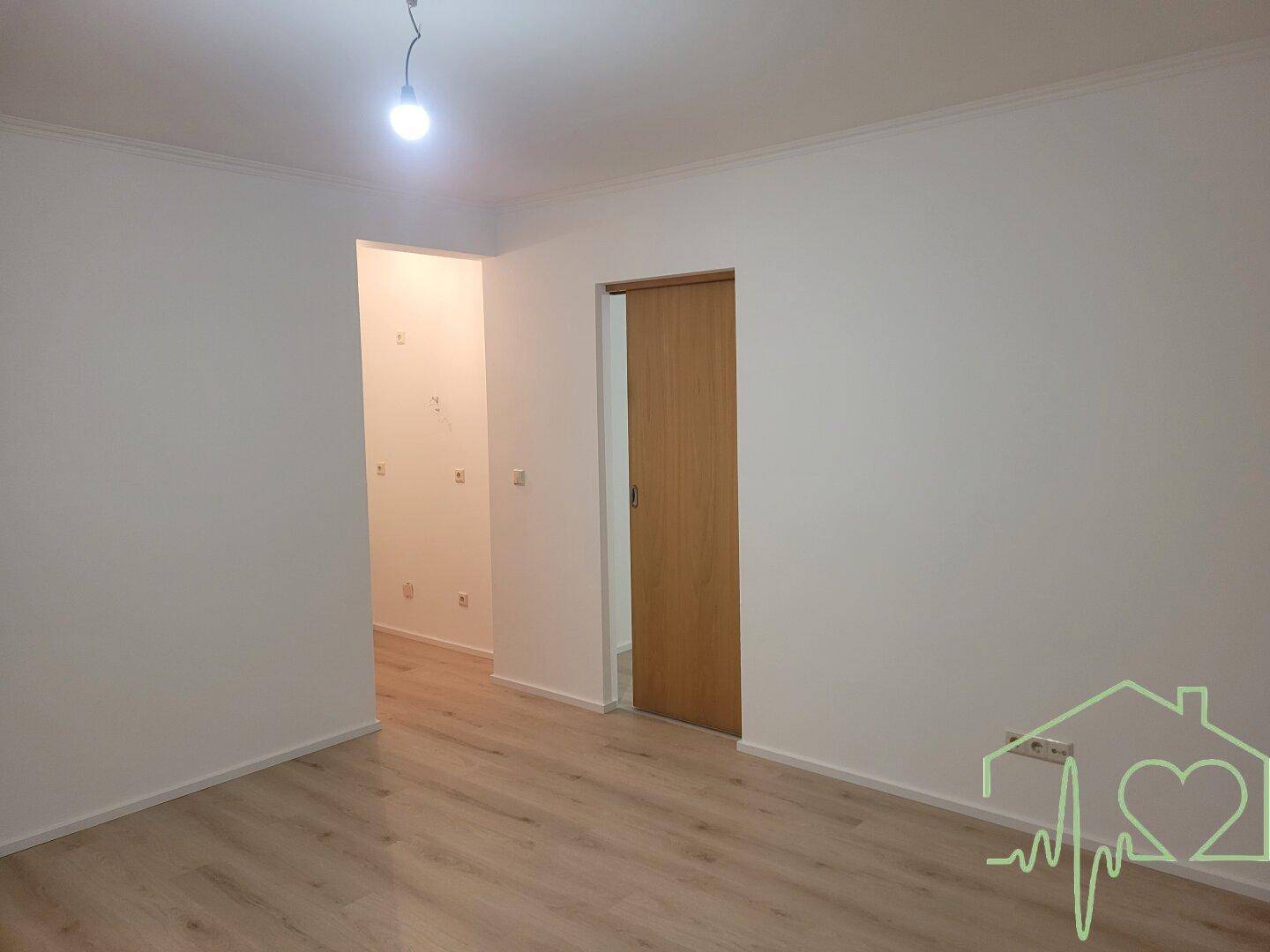 Heller Wohnraum mit Laminatboden und einer modernen Holzschiebetür, die zu einem weiteren Zimmer führt.