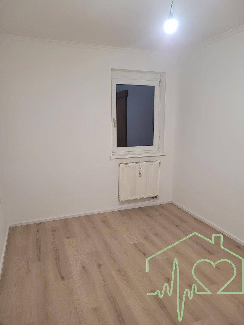 Helles Schlafzimmer mit Laminatboden und einem Fenster, das viel Tageslicht hereinlässt.