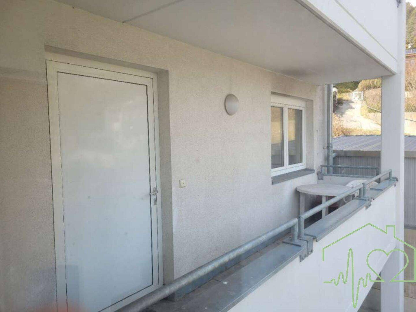 Detailansicht des Balkons mit Zugangstür und Fenster, ausgestattet mit einem kleinen Tisch.