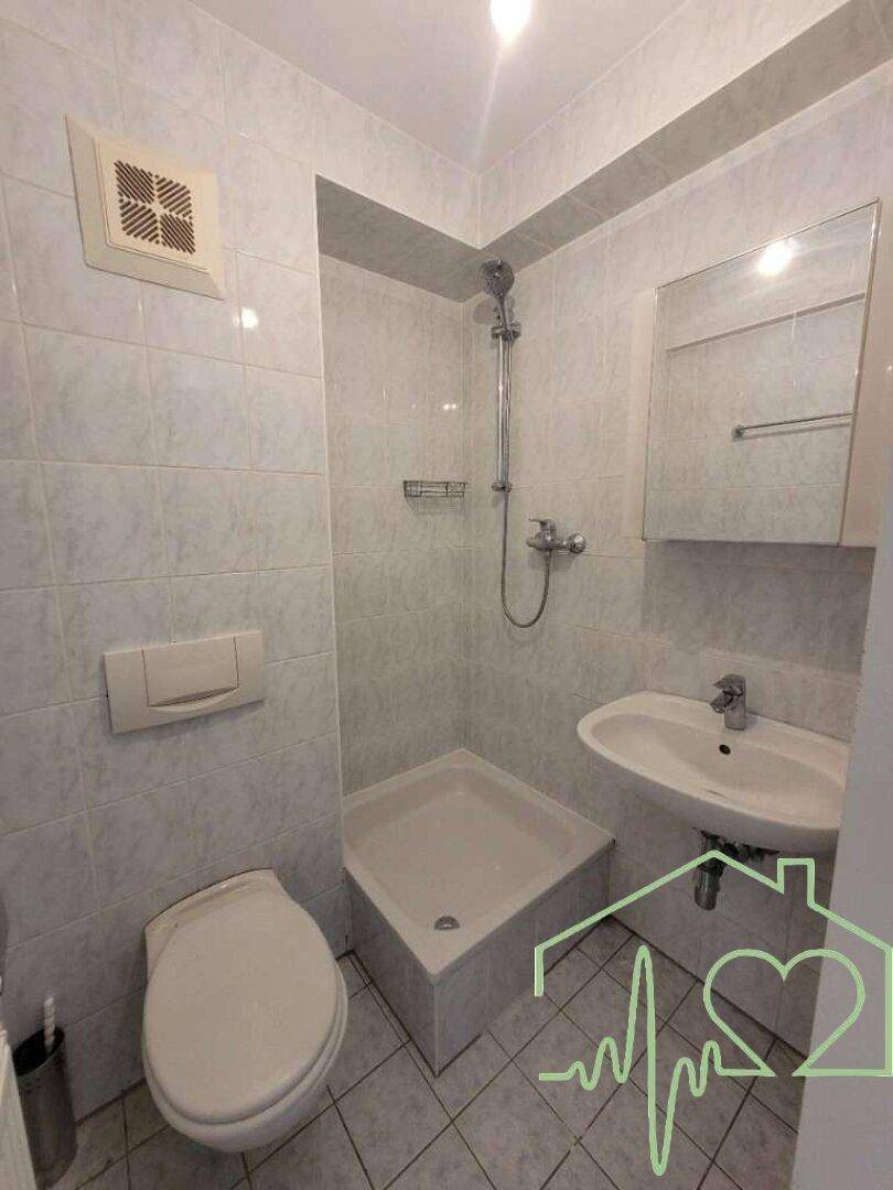Funktionales Badezimmer mit Dusche, WC, Waschbecken und hellen Fliesen, ausgestattet mit Spiegelschrank.