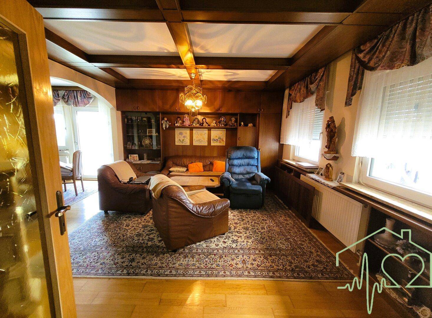 Gemütliches Wohnzimmer mit dunkler Holzvertäfelung, Holzbalkendecke und traditionellen Möbeln.