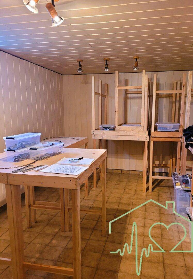 Werkstattraum mit Holztischen, Regalen und einfacher Deckenverkleidung.