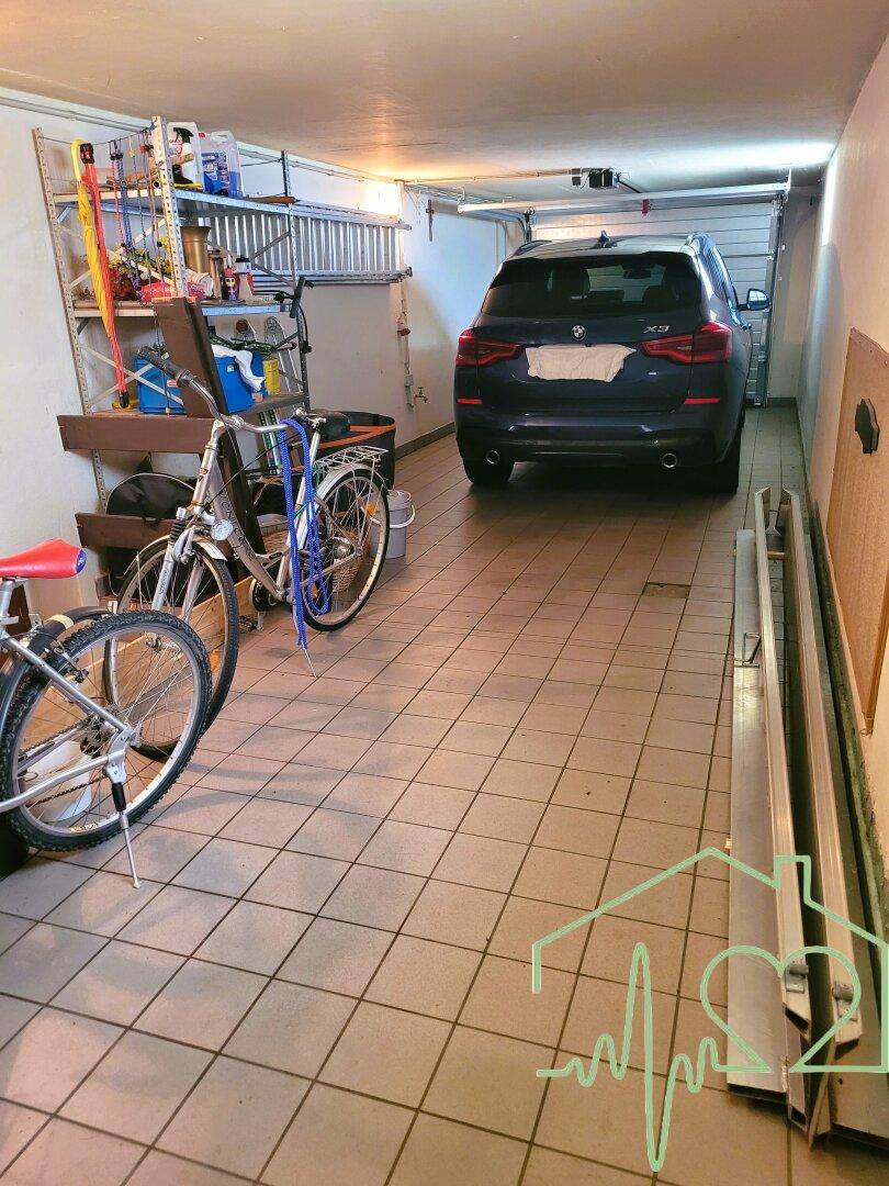 Geräumige Garage mit Fliesenboden, Abstellregalen und Platz für ein Auto und Fahrräder.