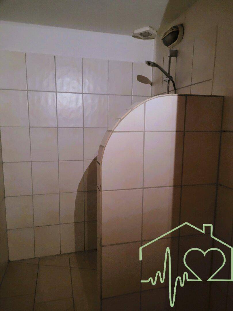 Duschbereich im Badezimmer mit weißen Fliesen und einer gemauerten Trennwand, schlicht und sauber.