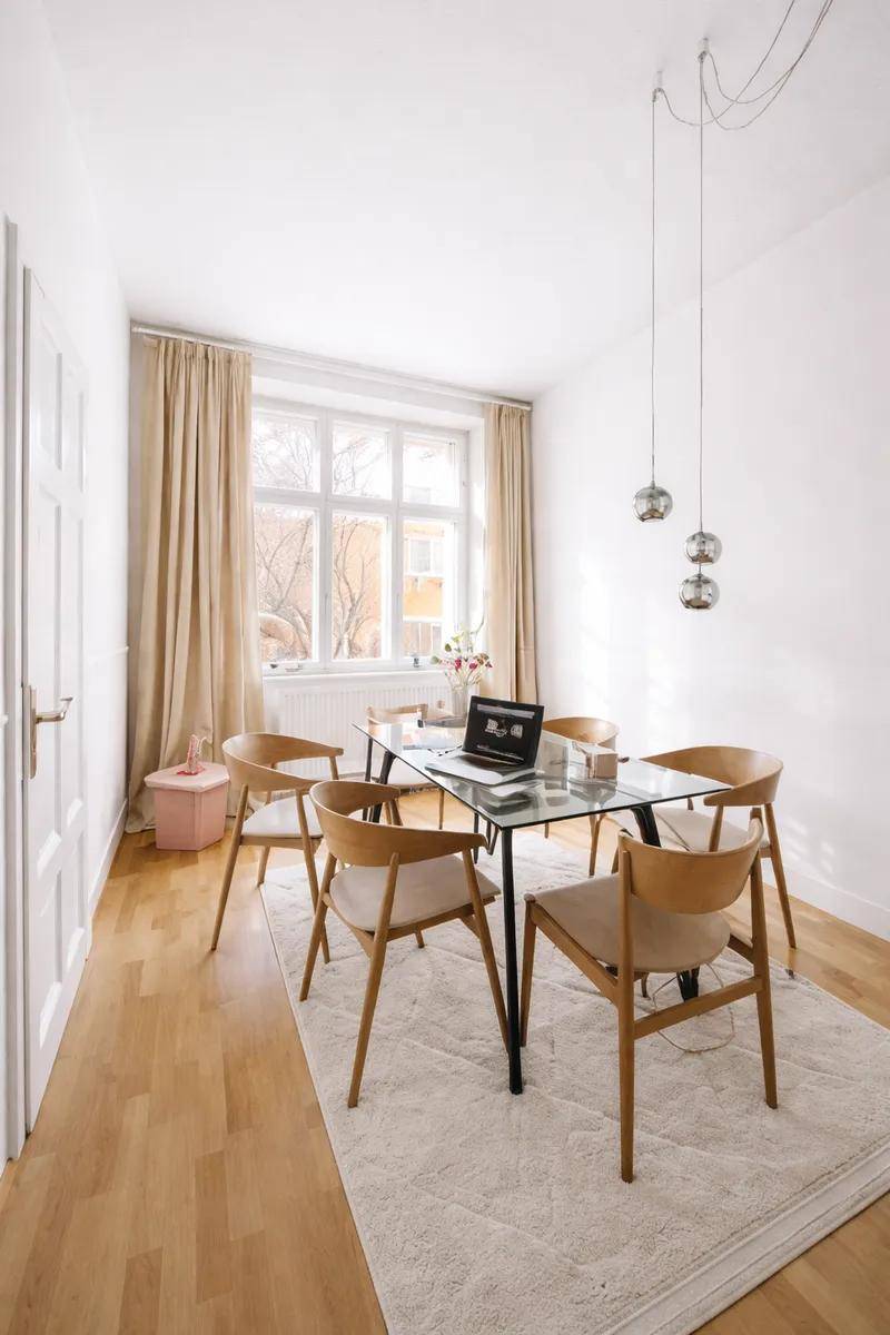 Heller Essbereich mit Holzboden, modernem Glastisch und Holzstühlen, beleuchtet durch ein großes Fenster.