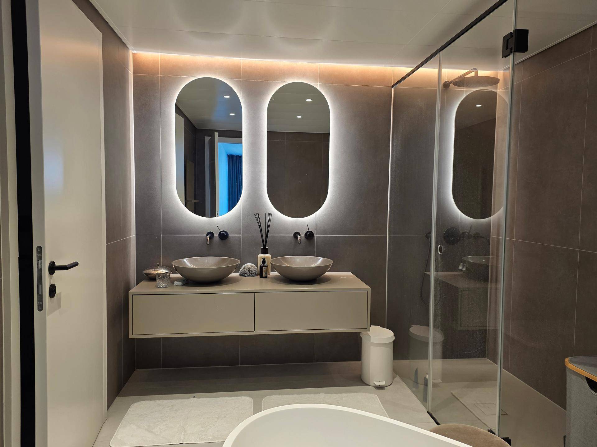 Modernes Badezimmer mit Doppelwaschbecken, beleuchteten Spiegeln und begehbarer Dusche.