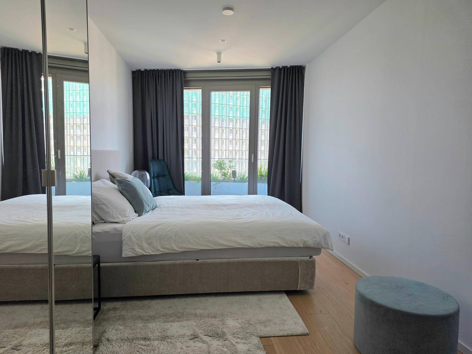 Helles Schlafzimmer mit Holzboden und großem Fenster, das viel Tageslicht hereinlässt.