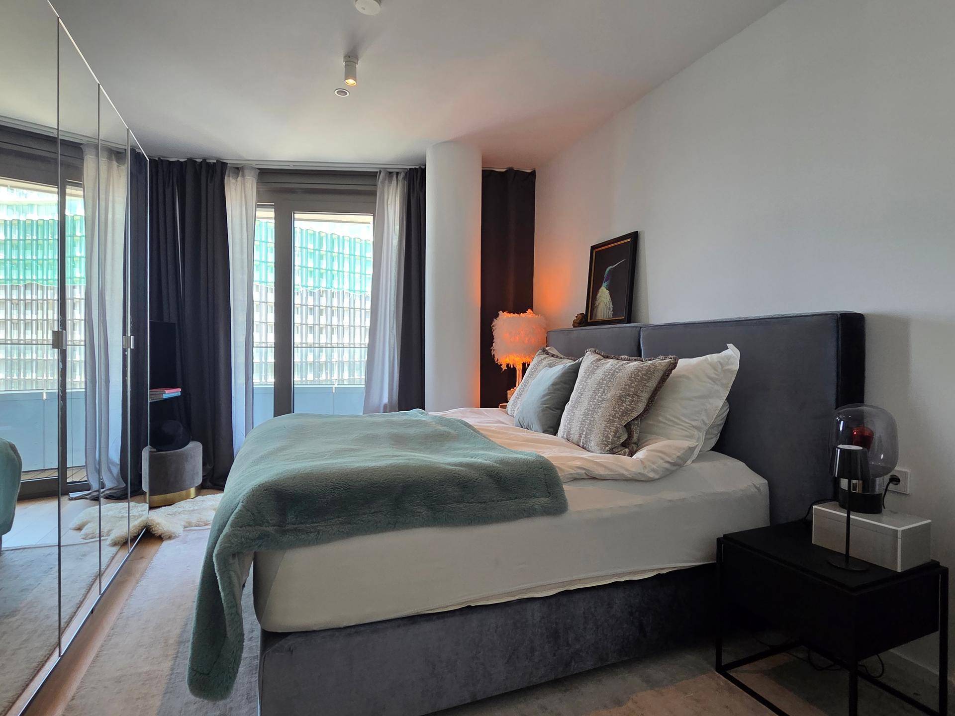 Gemütliches Schlafzimmer mit großem Bett, Spiegelschrank und Zugang zu einem Balkon.