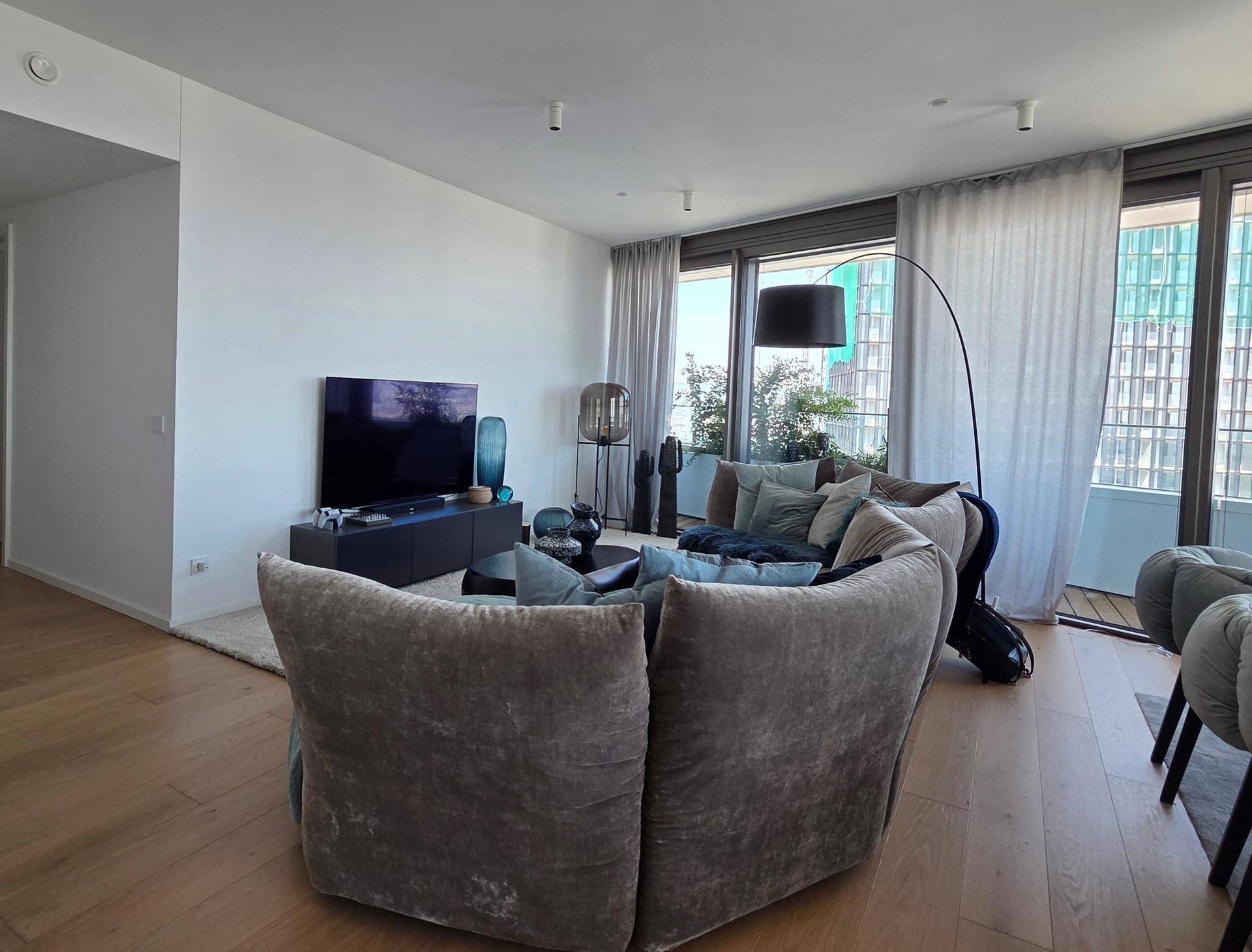 Geräumiges Wohnzimmer mit großem Sofa, Fernseher und bodentiefen Fenstern.