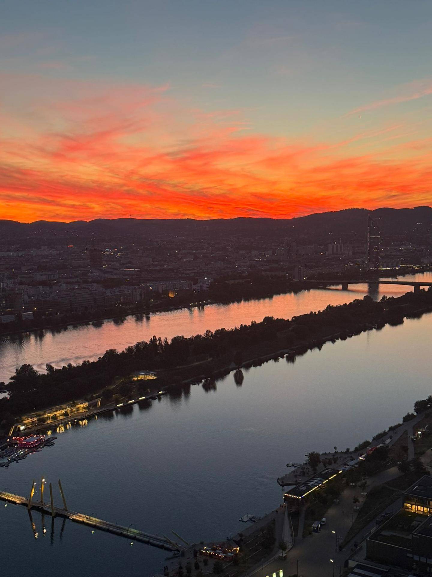 Spektakulärer Sonnenuntergang über der Stadt und dem Fluss mit leuchtend rotem Himmel.