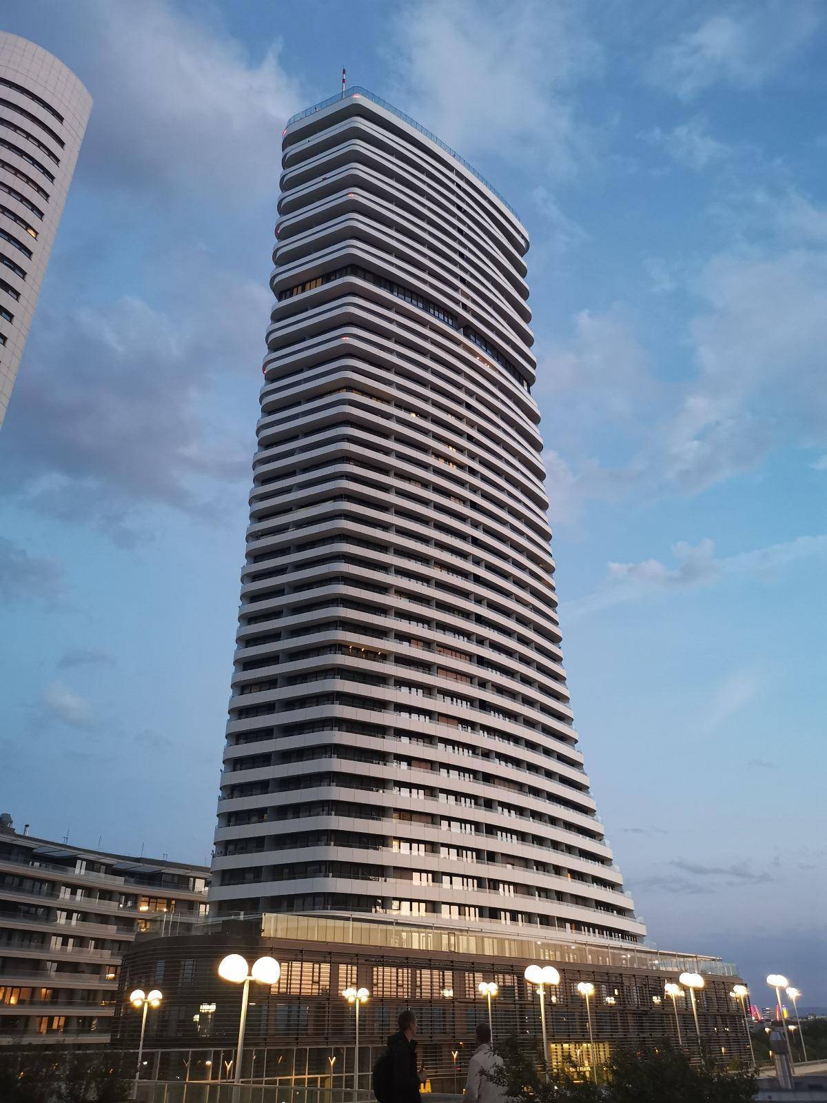 Elegantes Hochhaus bei Sonnenuntergang mit markanter Architektur und Wolkenhimmel.