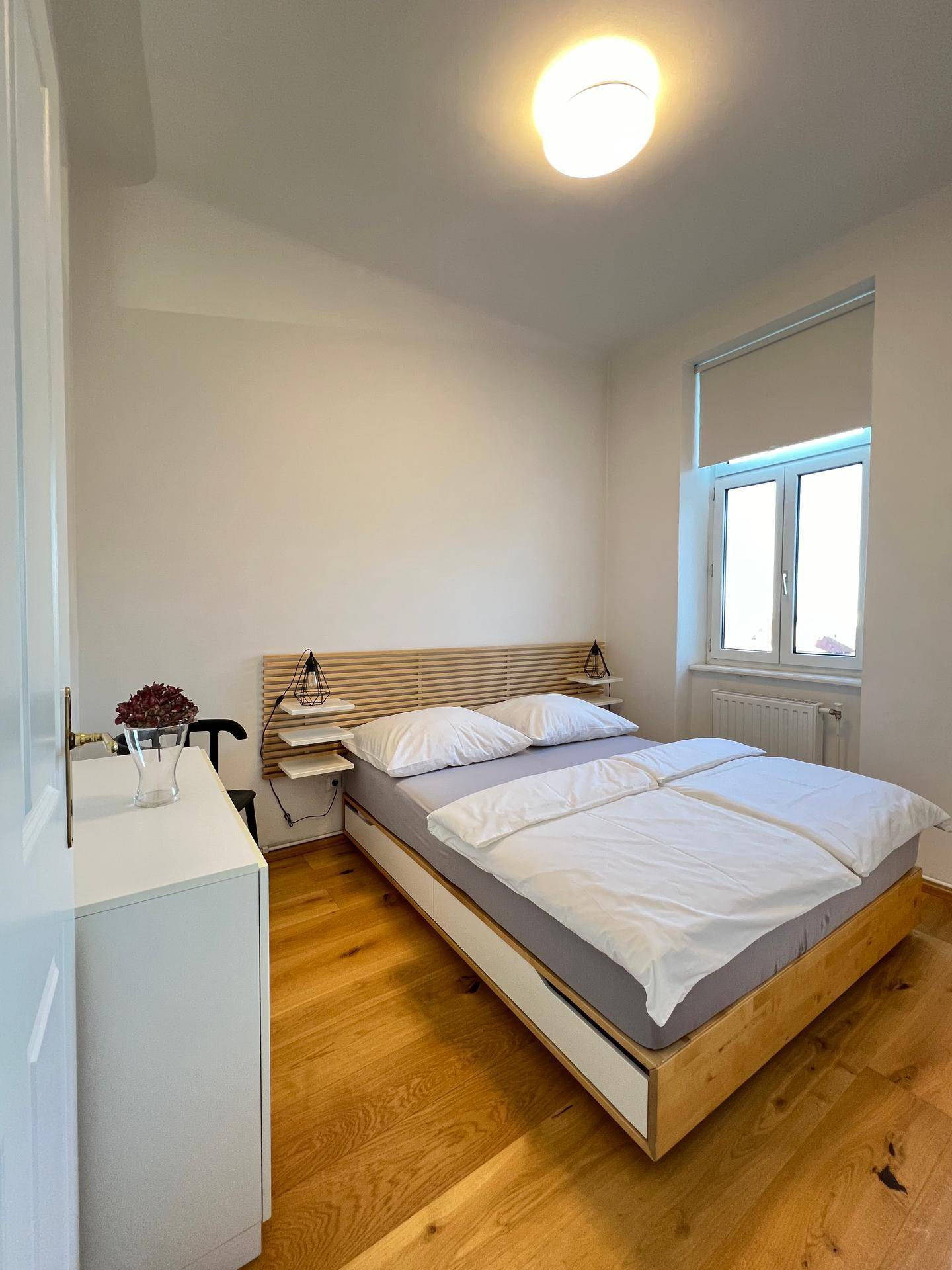 Helles Schlafzimmer mit Holzbett, Parkettboden und einem Fenster für viel Tageslicht.