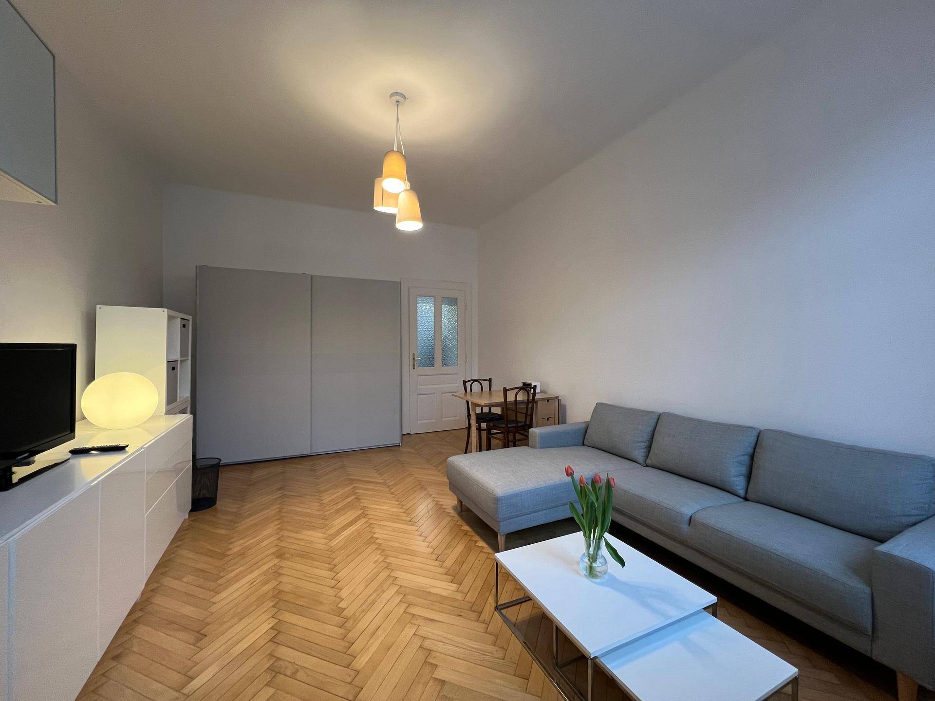 Geräumiges Wohnzimmer mit bequemer Couch, TV-Möbeln und elegantem Fischgrätparkettboden.