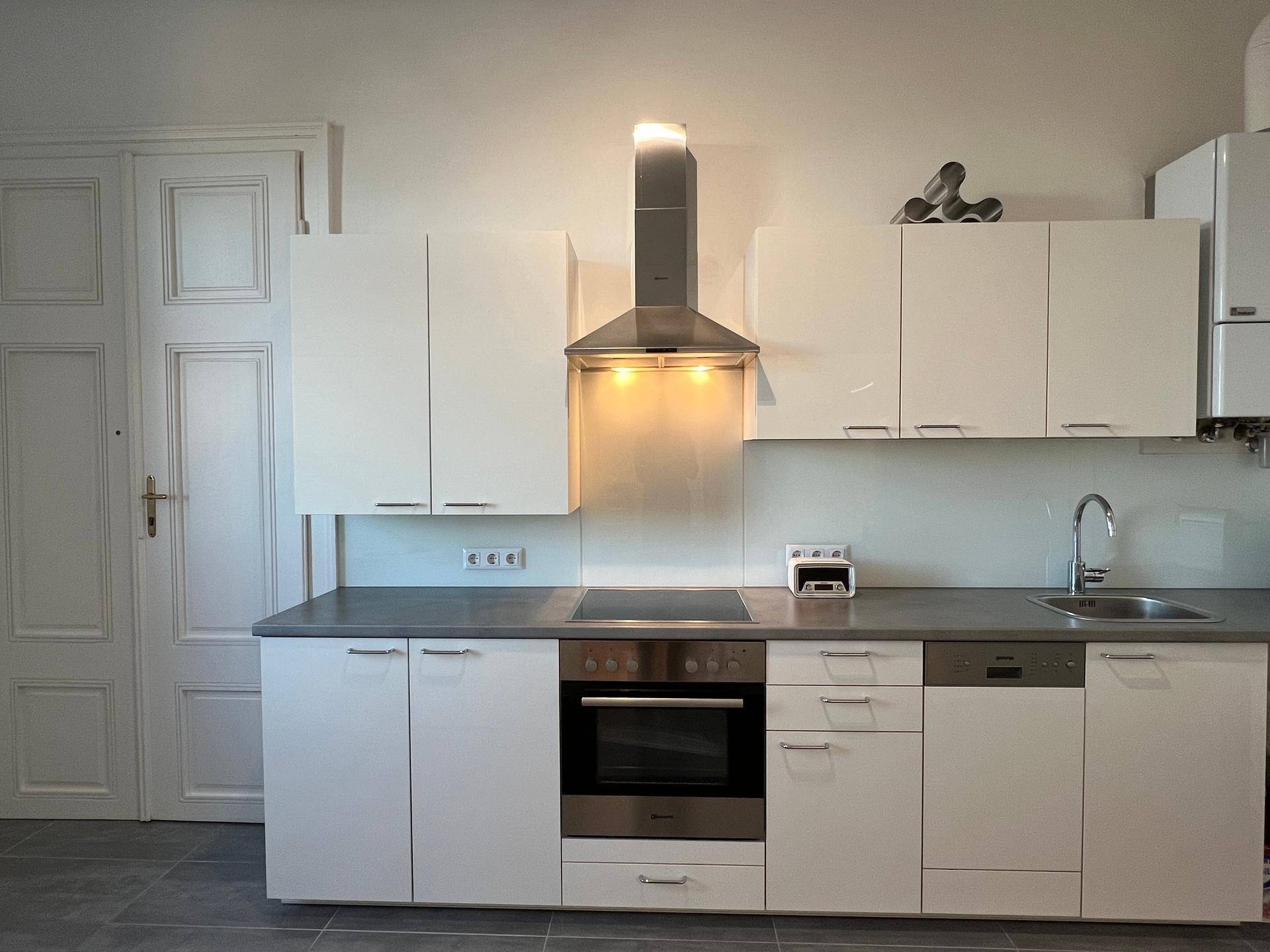 Moderne Einbauküche mit weißen Hochglanzfronten, integriertem Backofen und Dunstabzugshaube.