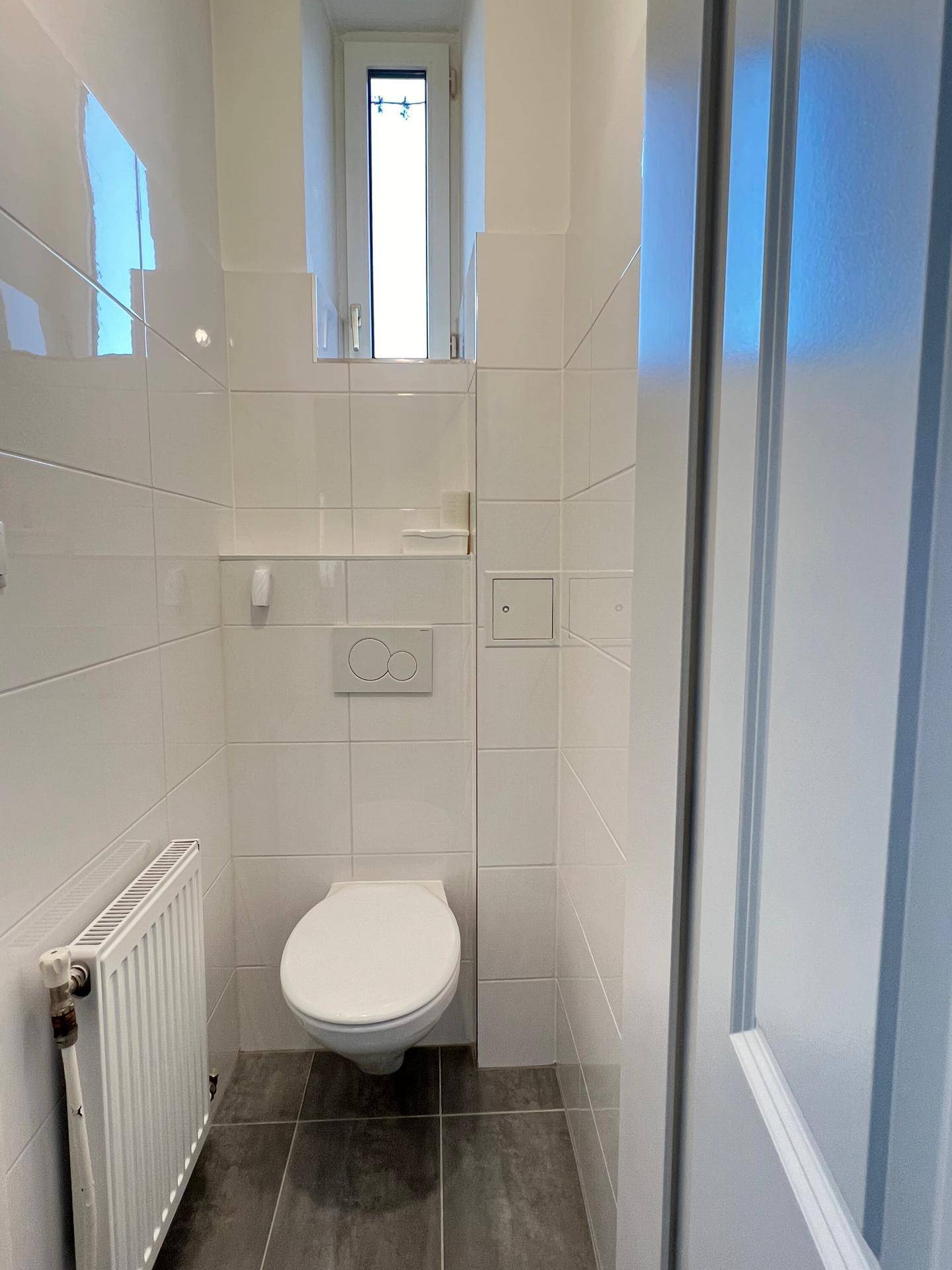 Separates WC mit Wand-WC, Heizung und kleinem Fenster für Belüftung.