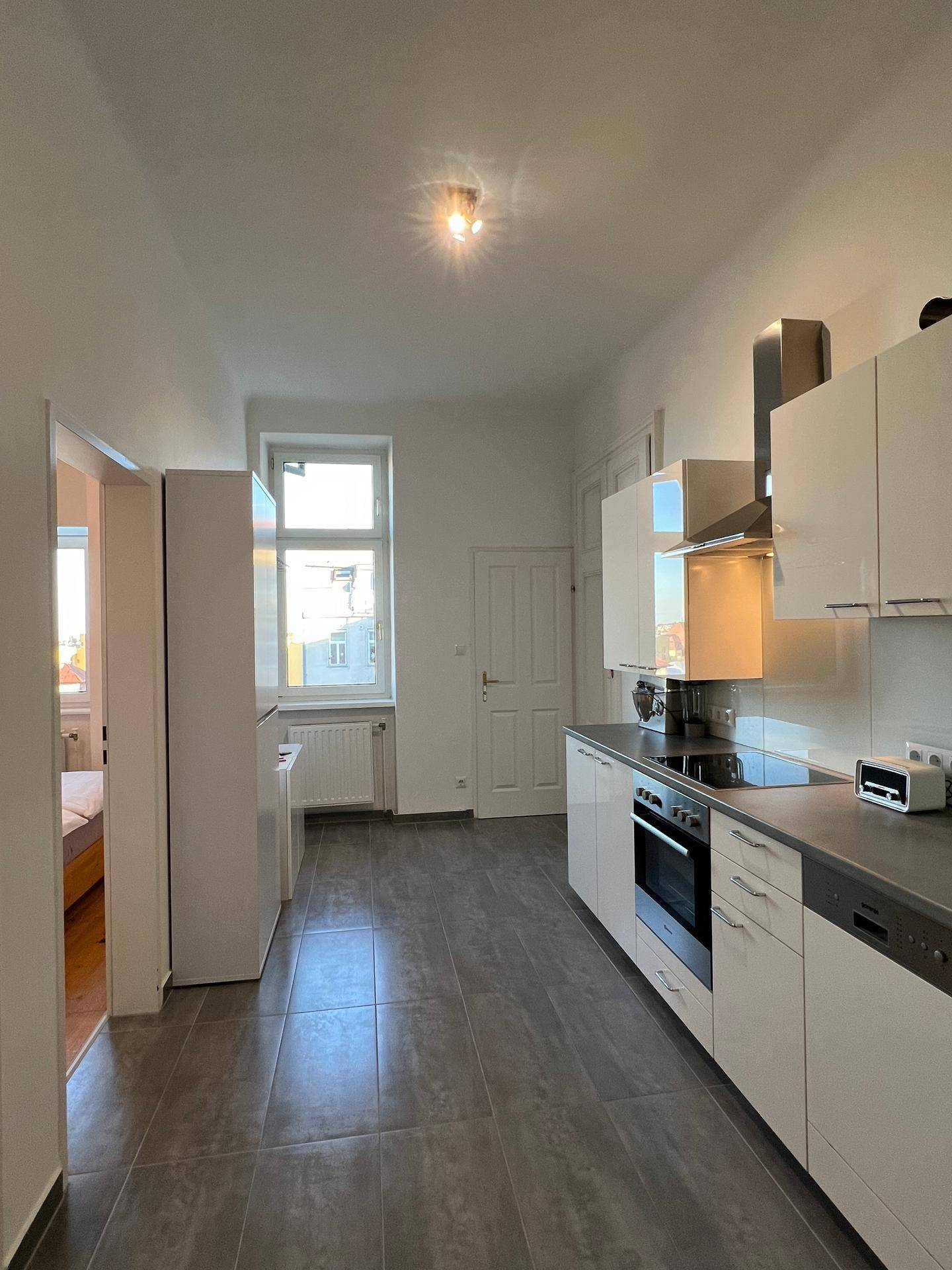 Geräumige Küche mit Fliesenboden, weißen Schränken und einem Fenster für natürliches Licht.