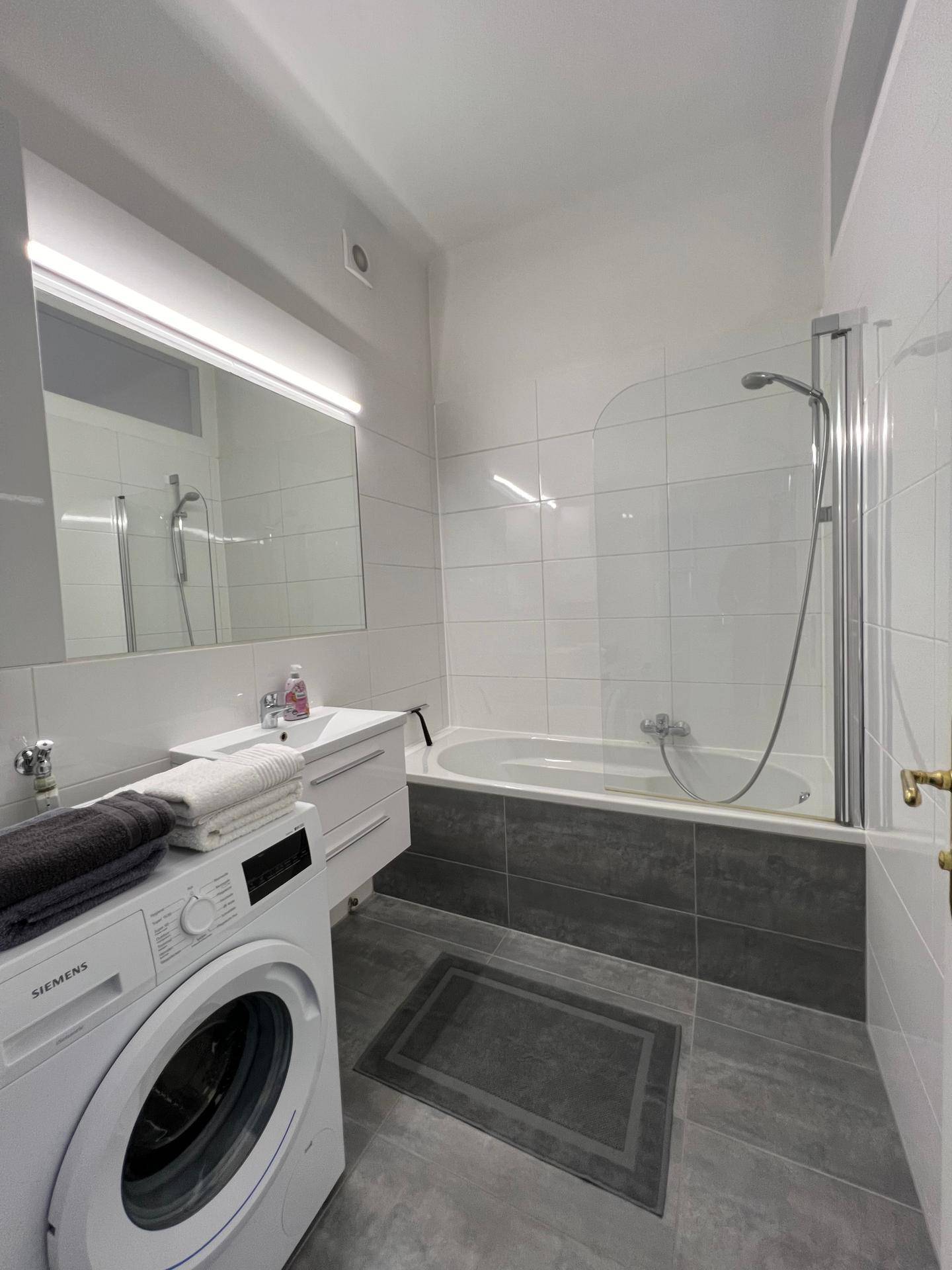 Modernes Badezimmer mit Badewanne, Dusche und Waschmaschine, hell gefliest.