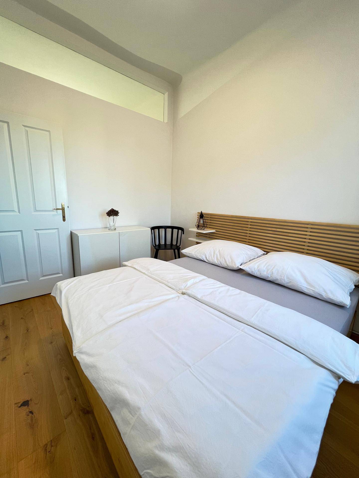 Ruhiges Schlafzimmer mit Doppelbett, Holzboden und schlichter, moderner Einrichtung.