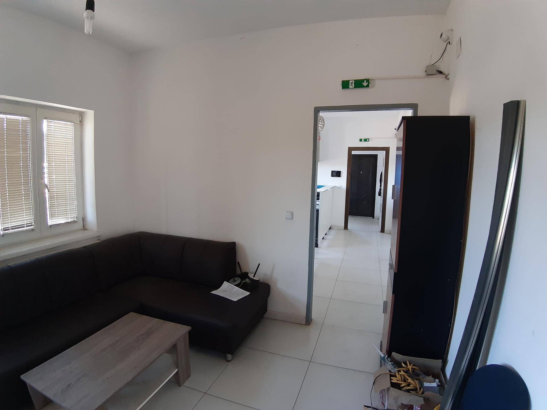 Einfacher Büroraum oder Aufenthaltsraum mit Sofa, Couchtisch und Fliesenboden.