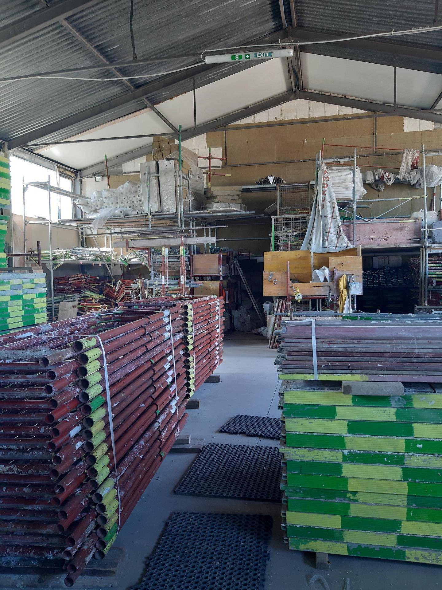 Lagerhalle mit hohen Stapeln von Baumaterialien und einem Notausgangsschild an der Decke.