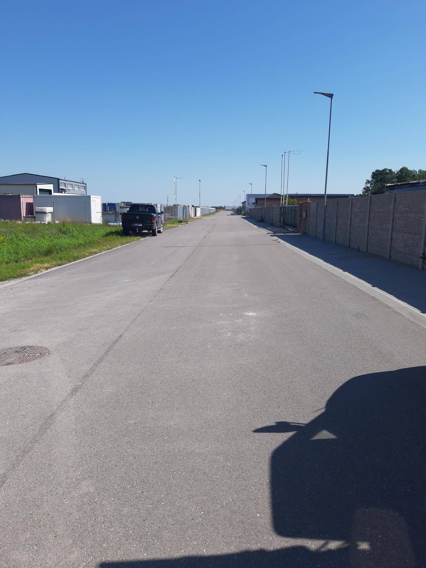 Lange, gerade Straße in einem Industriegebiet mit Gebäuden und Zäunen entlang der Seiten unter blauem Himmel.