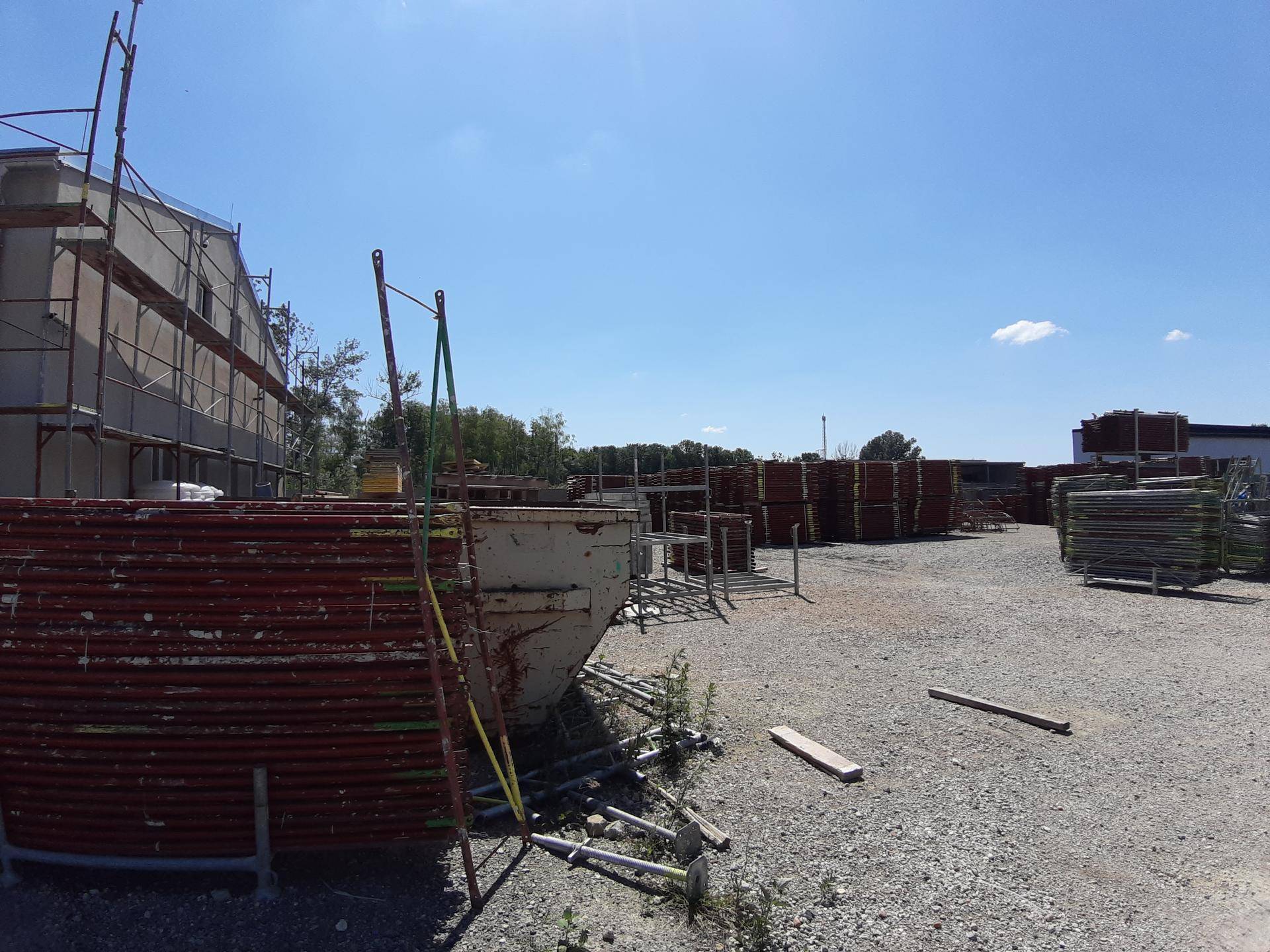Außenlagerplatz mit Gerüstmaterialien, einem Container und einem Gebäude im Hintergrund.