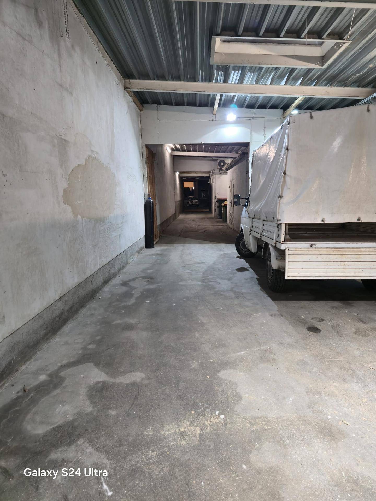 Schmaler Industrieraum mit Betonboden und einem geparkten Lieferwagen, führt zu einem hinteren Gang.