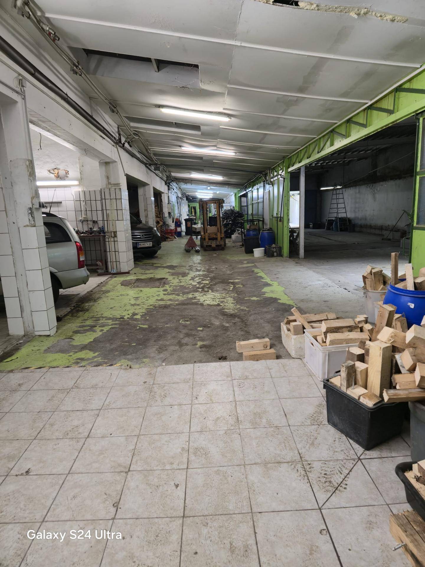 Geräumige Werkstatt oder Garage mit Fliesenboden im Vordergrund und Fahrzeugen sowie Geräten im Hintergrund.