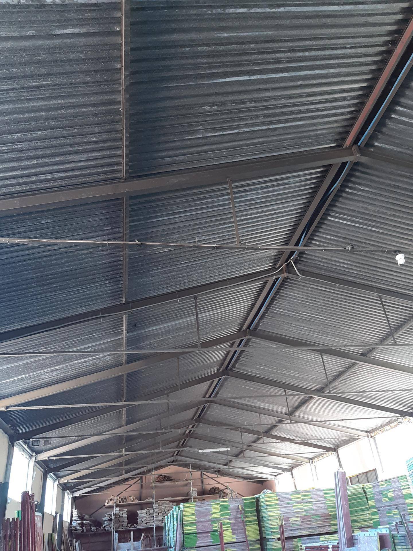 Blick auf das Wellblechdach und die Metallkonstruktion einer Lagerhalle mit sichtbaren Trägern.