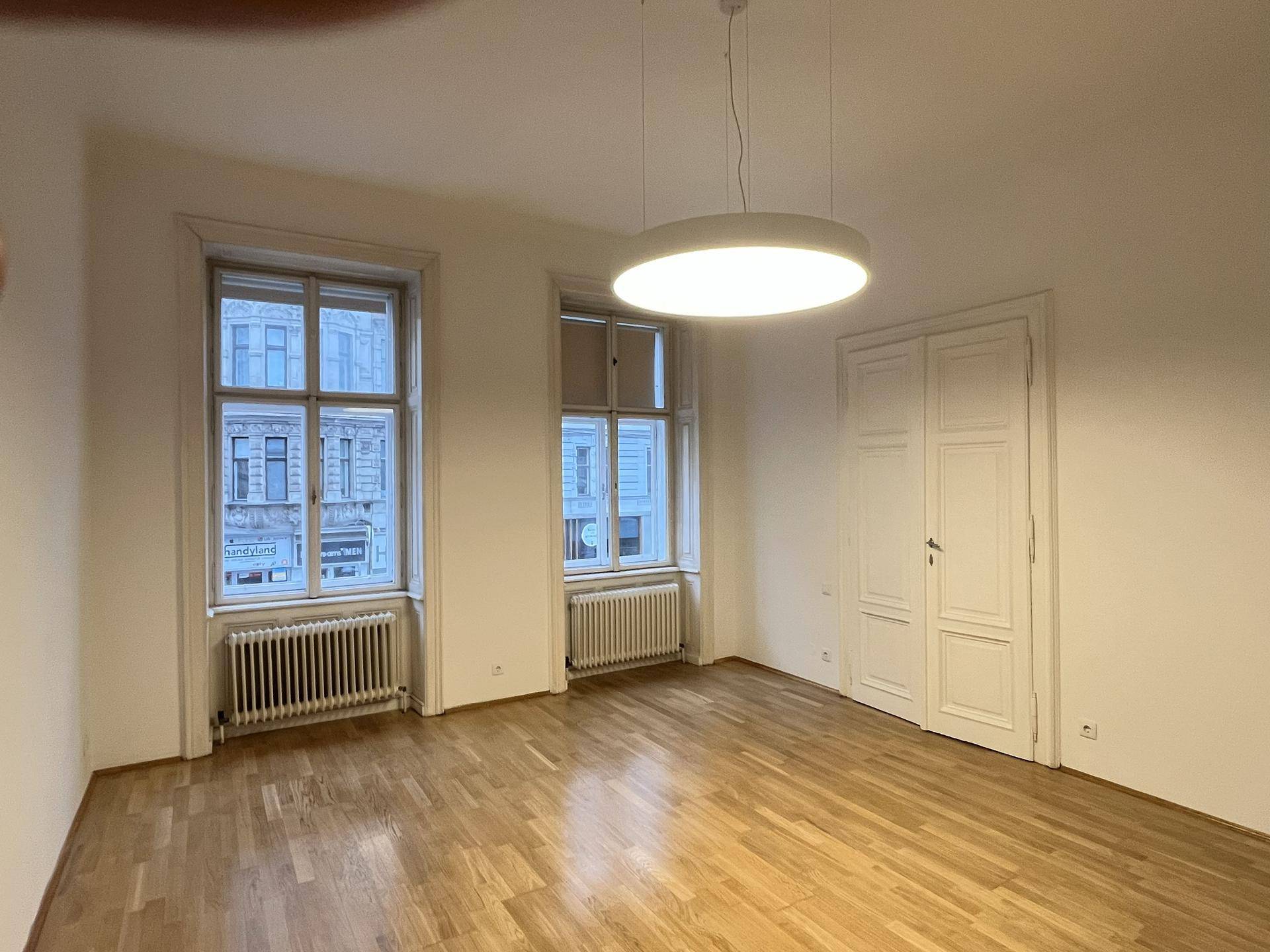 Heller Wohnraum mit hohen Decken, Parkettboden und großen Fenstern mit Blick auf die Stadt.