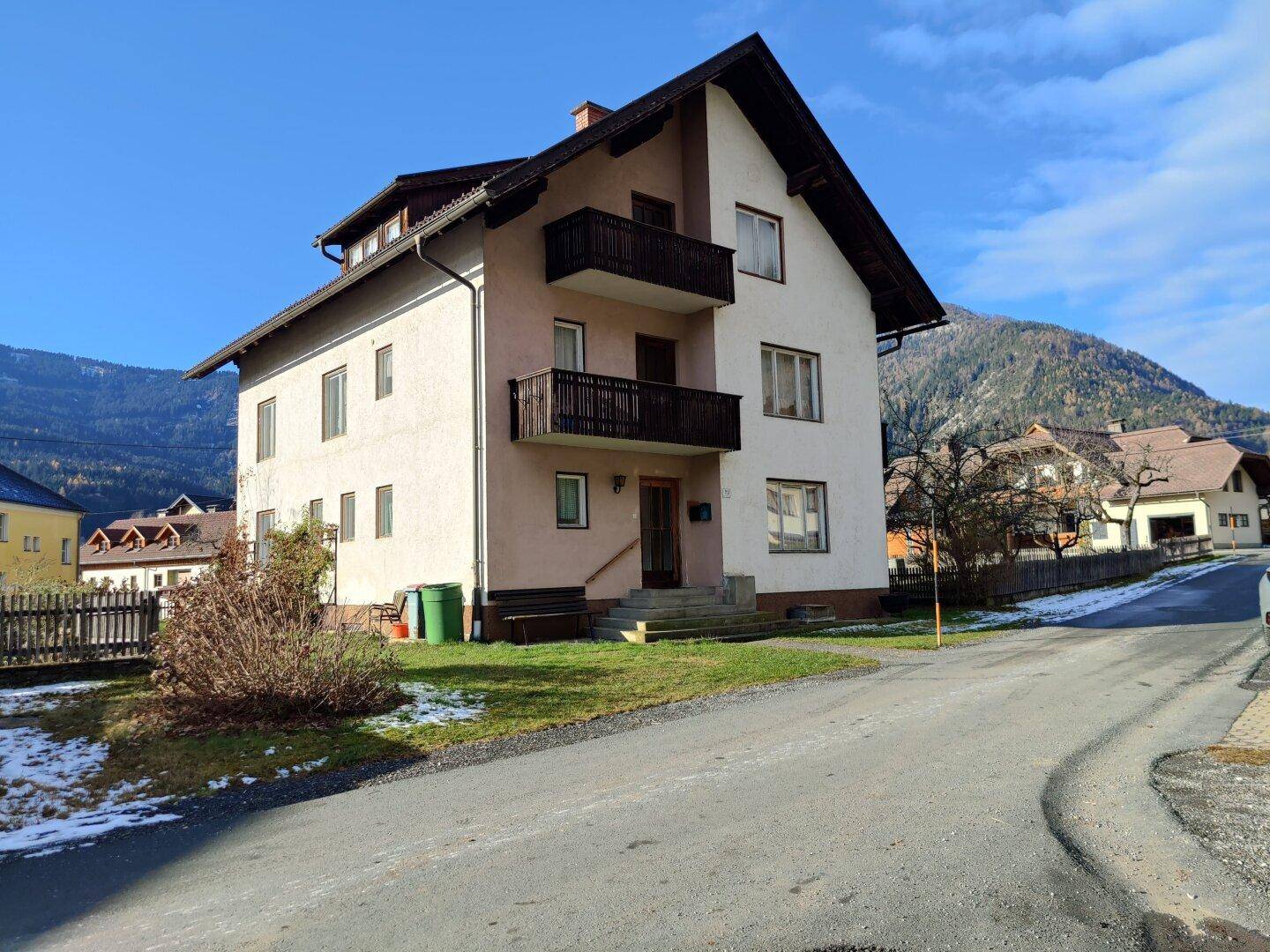Ansicht des Wohnhauses von der Straße mit Balkonen und umliegender Berglandschaft im Winter.