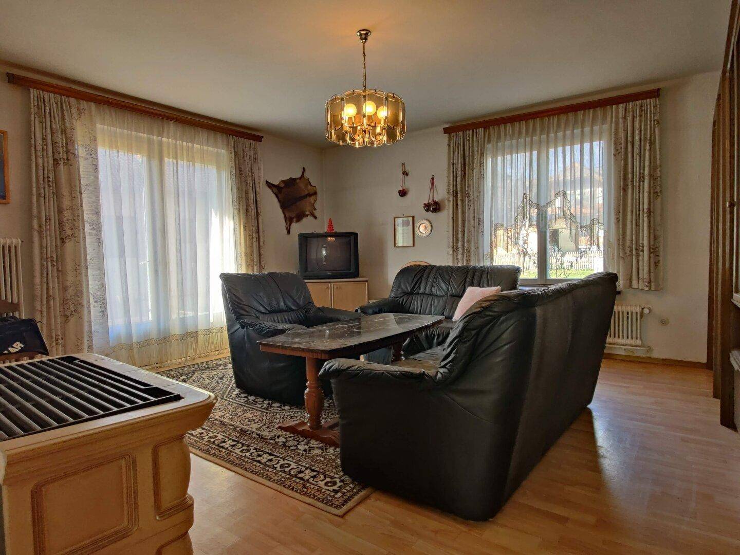 Gemütliches Wohnzimmer mit dunklen Ledersofas, Parkettboden und traditionellem Kachelofen.