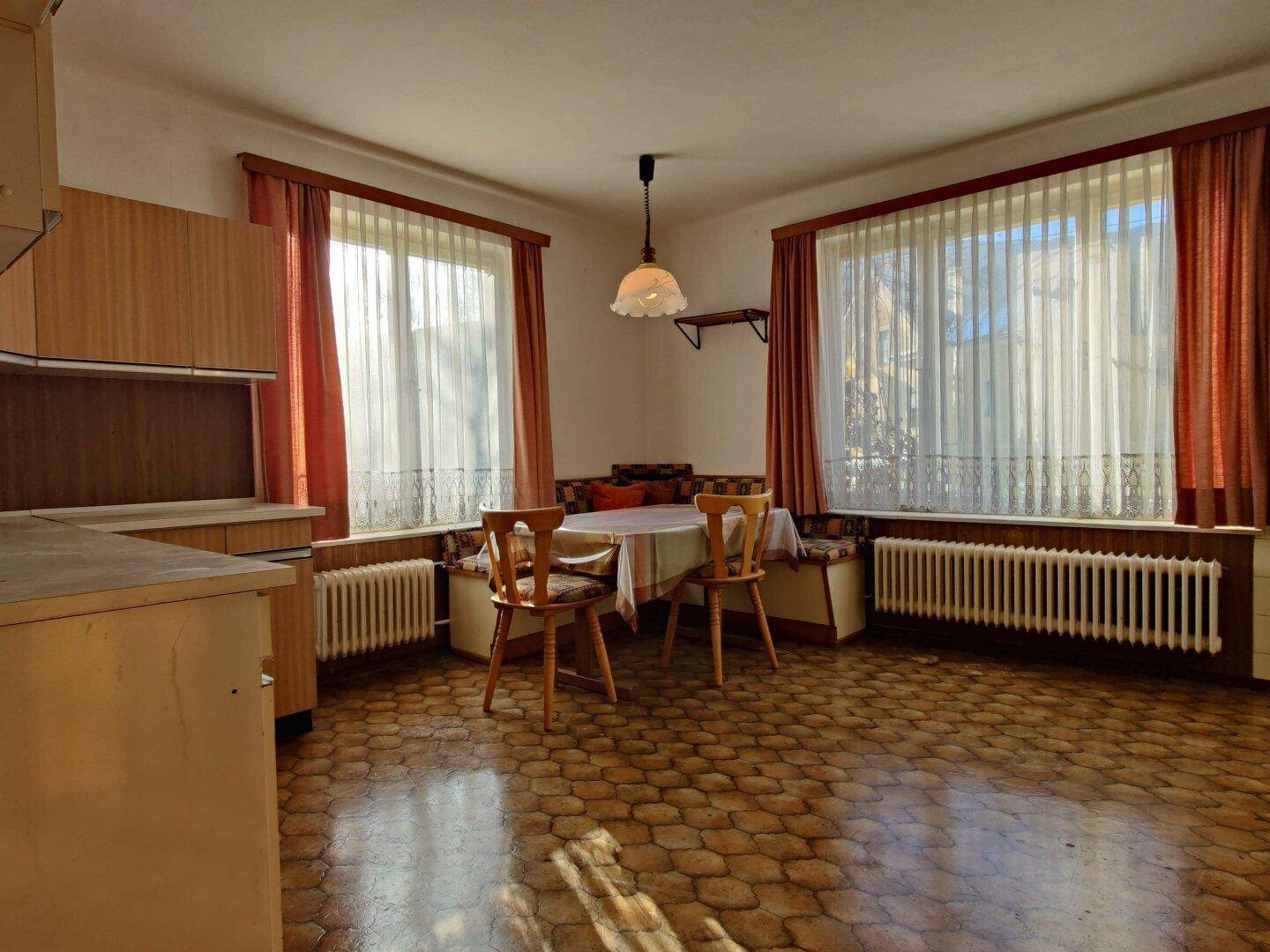 Helle Küche mit Essbereich, älteren Einbaumöbeln und gemustertem Fliesenboden.