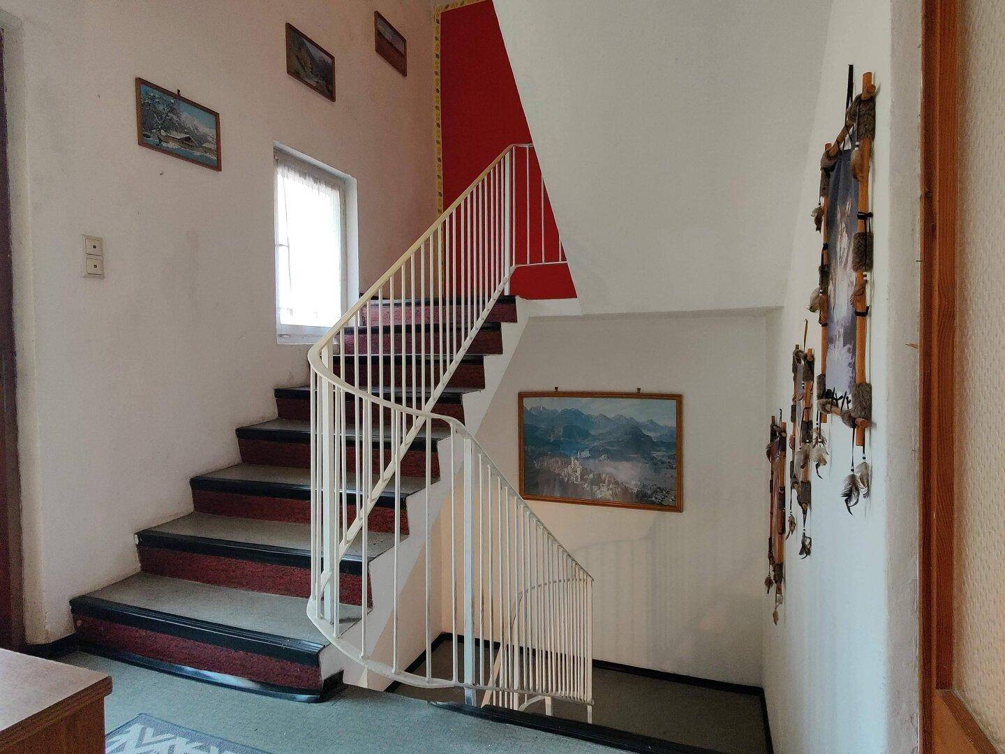Treppenhaus mit weißem Geländer, rotem Akzent und traditioneller Dekoration.